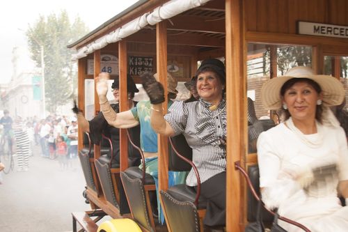 Pasajeras de época saludan desde uno de los vehículos de la caravana, a su paso por Melo